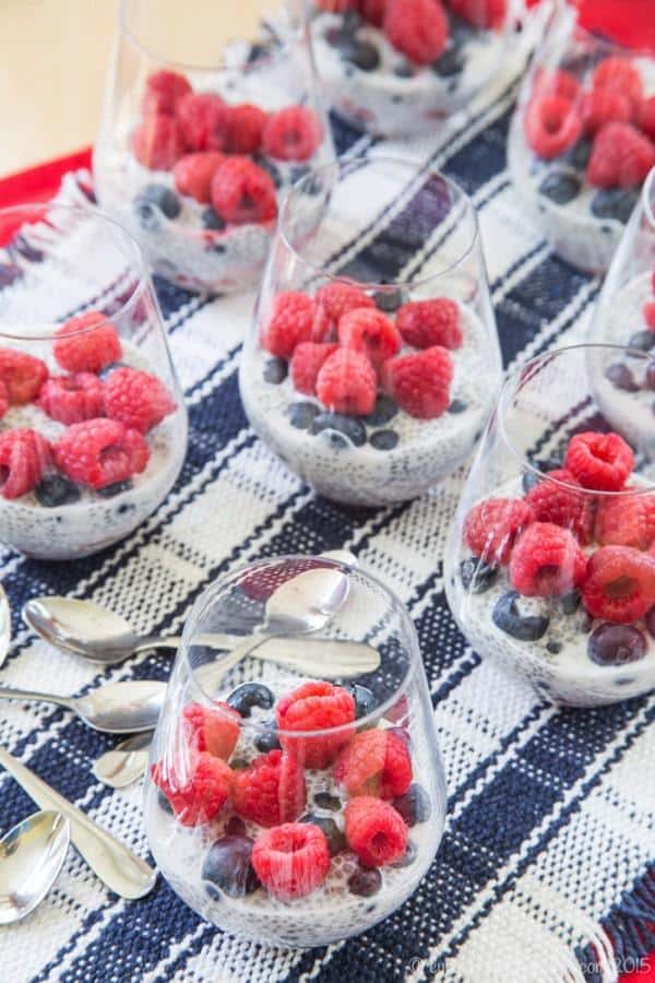 Wine glasses filled with Triple Berry Coconut Chia Pudding Parfaits with beautiful fresh raspberries on top
