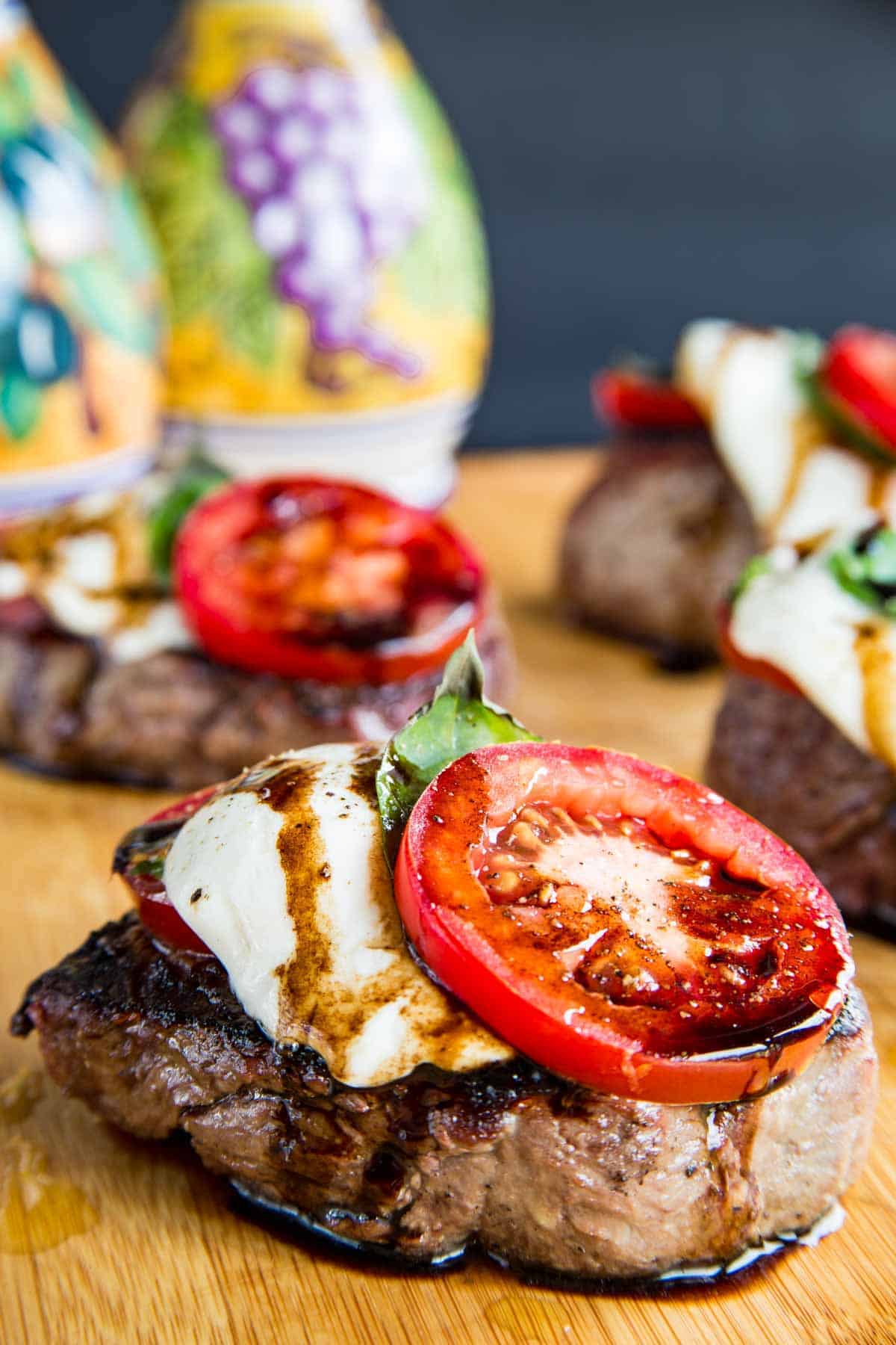 grilled filet mignon steak topped with fresh mozzarella, a basil leaf, a slice of tomato, and a drizzle of balsamic vinegar