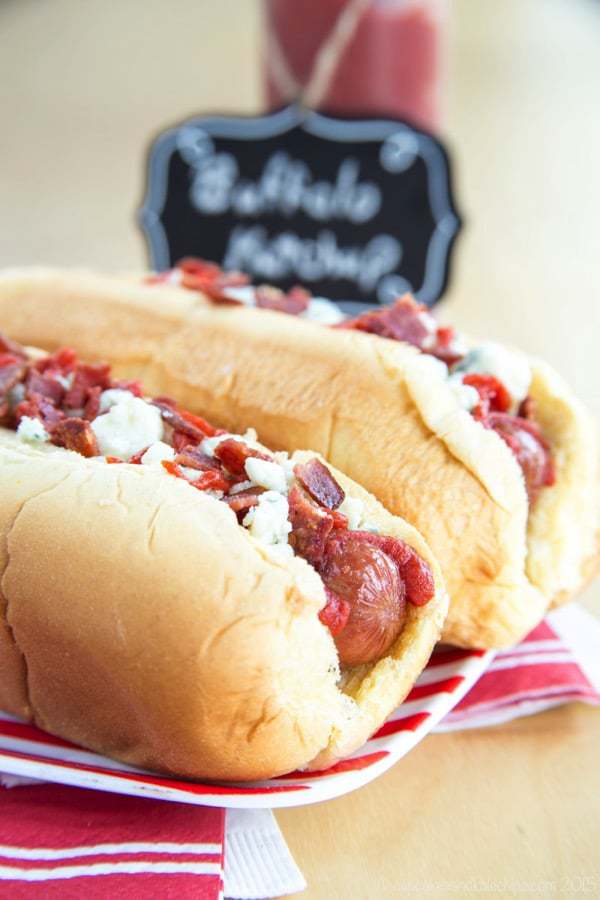 Closeup of Buffalo, Bacon, and Blue Cheese Hot Dogs in a bun on a red and white striped plate