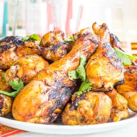 grilled tandoori chicken drumsticks on a plate with glasses of wine and orange and yellow plates behind it