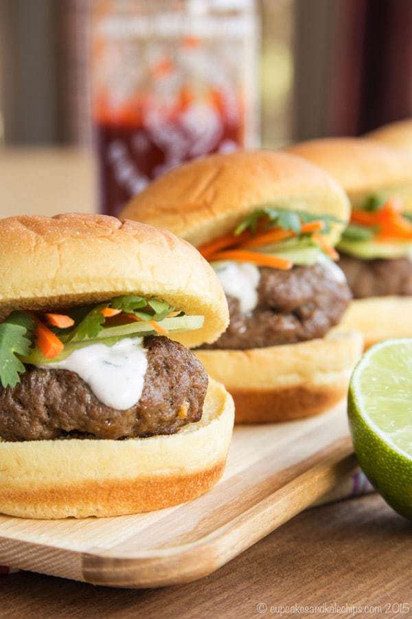 Mini Thai Burgers topped with cucumbers, carrots, and cilantro lime cream on a wooden platter