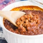 A spoonful of semi homemade baked beans scooped out of a white corningware dish