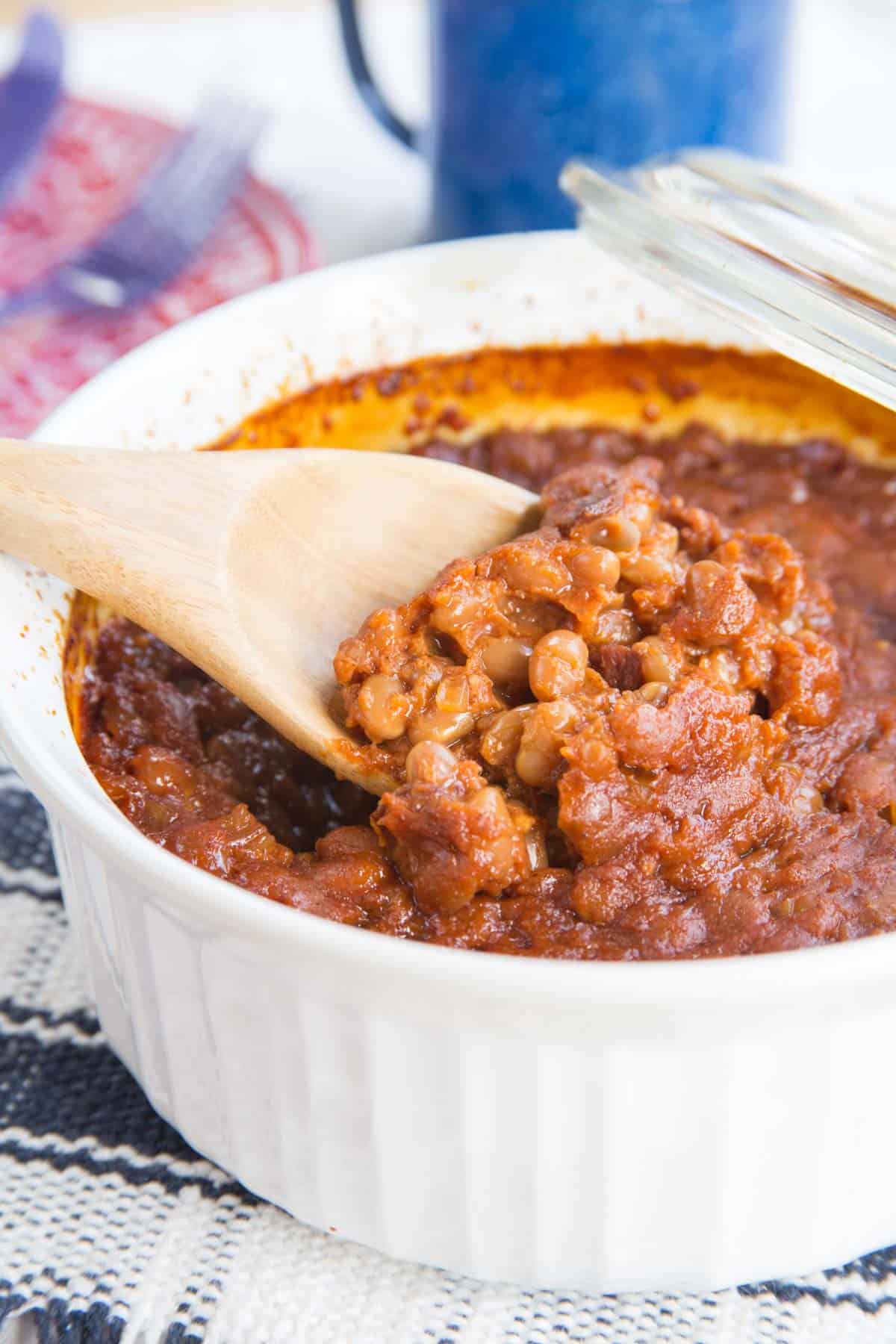 A spoonful of semi homemade baked beans scooped out of a white corningware dish