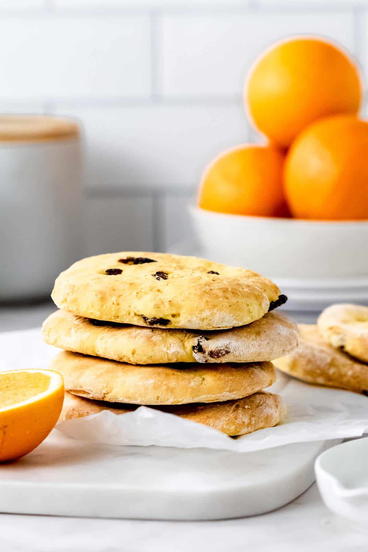 A stack of gluten-free cranberry orange pita bread next to half an orange on a white countertop.