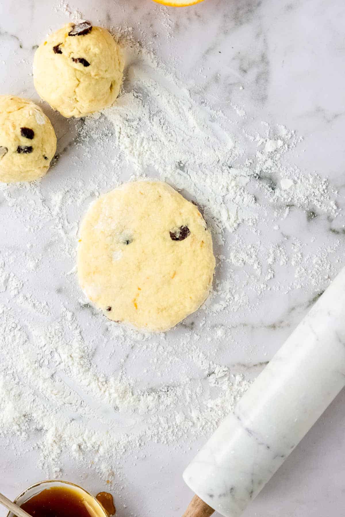 Cranberry orange pita bread dough is rolled into discs on a floured marble countertop.