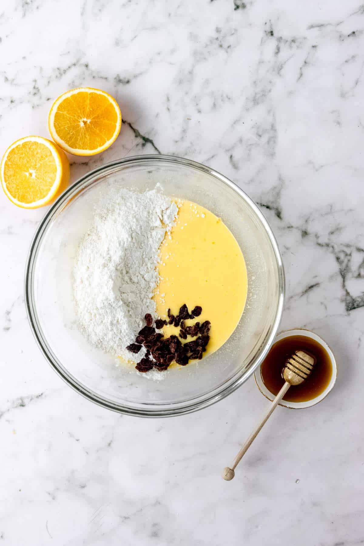 Dry ingredients and dried cranberries are added to the wet ingredients for gluten-free pita bread dough in a glass bowl.