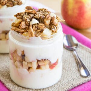 An apple yogurt parfait in a jar with a small spoon next to it.