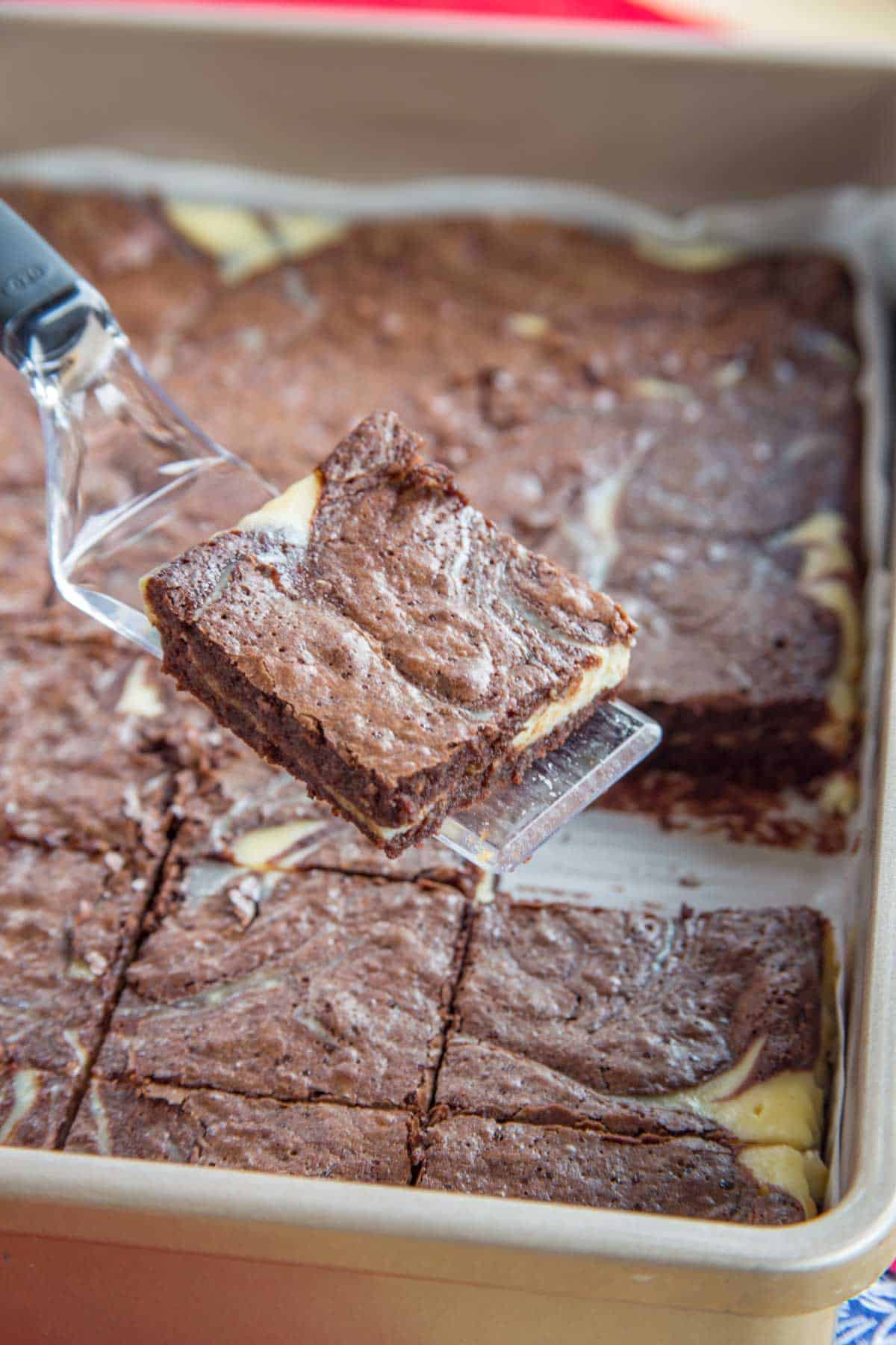 A spatula holding a cheesecake-swirled brownie over the pan of brownies.