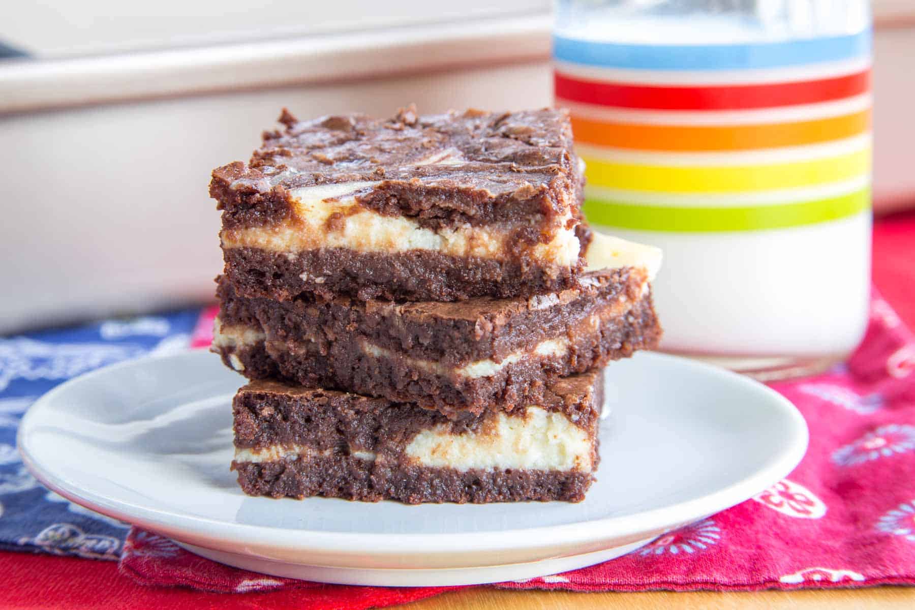 A stack of three brownies with a cheesecake swirl on a small white plate.