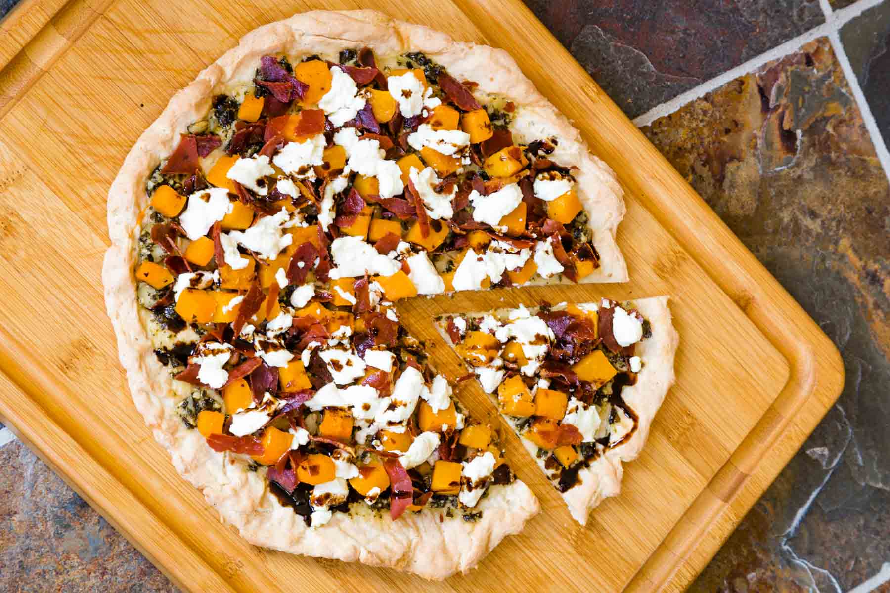 A whole gluten free pizza with butternut squash on a cutting board with one slice cut and pulled away slightly.