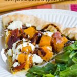 A slice of gluten free butternut squash pizza also topped with prosciutto and goat cheese with arugula on a white dish.