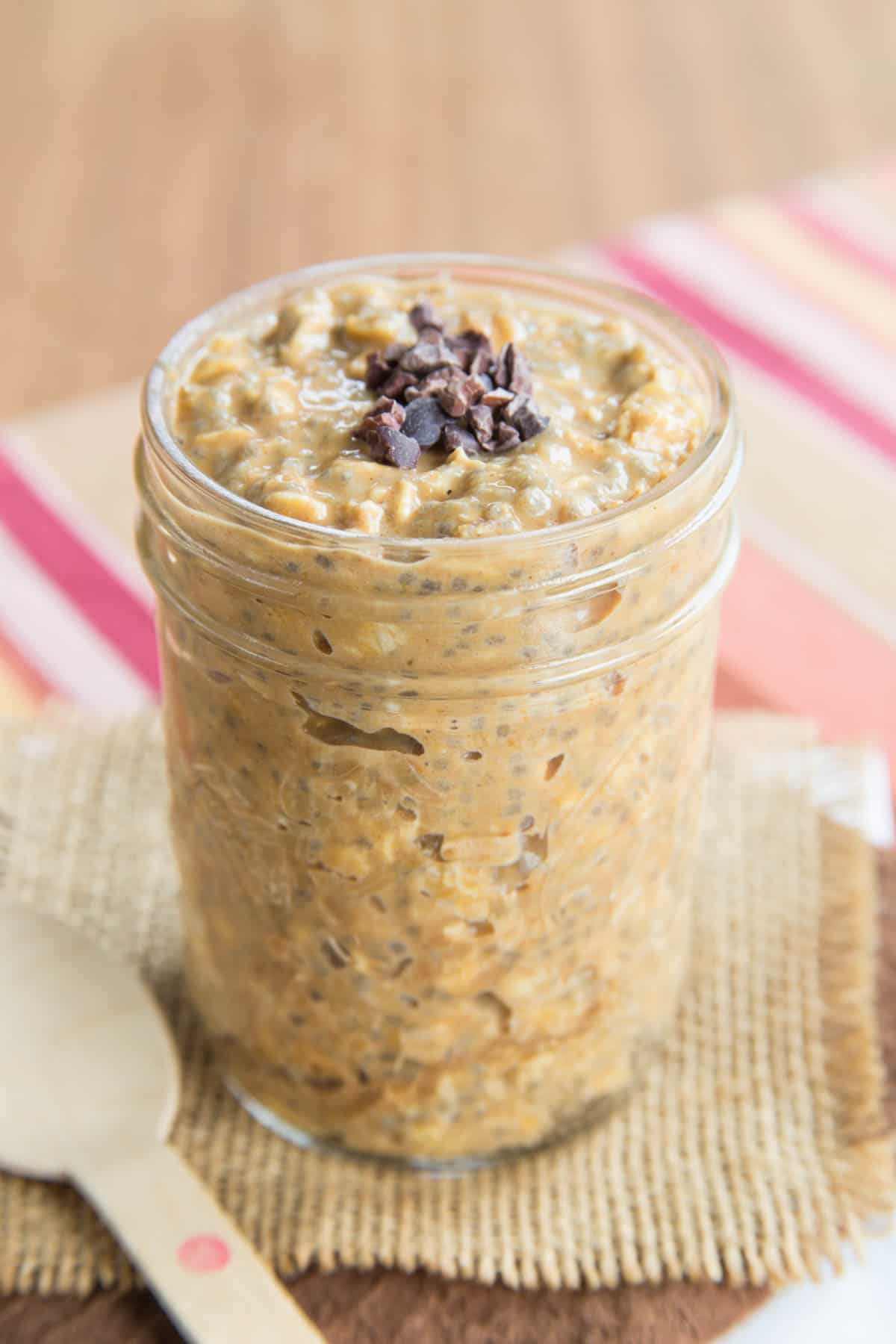 A jar of overnight oats with a light orange color due to pumpkin in the recipe and sprinkled with cacao nibs on top.