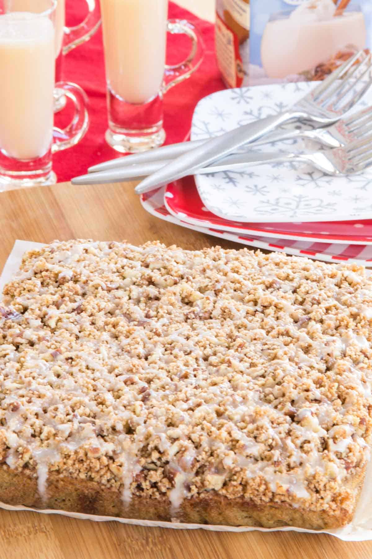 A whole crumb-topped coffee cake with an icing drizzle on a piece of parchment paper on a cutting board.