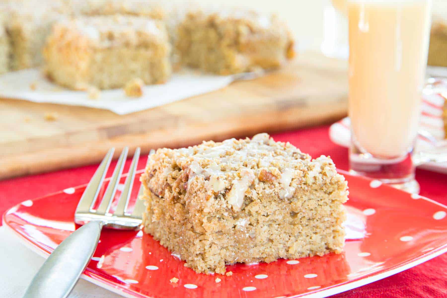 A piece of Gluten Free Eggnog Coffee Cake with a fork next to it on a red plate with white polka dots.