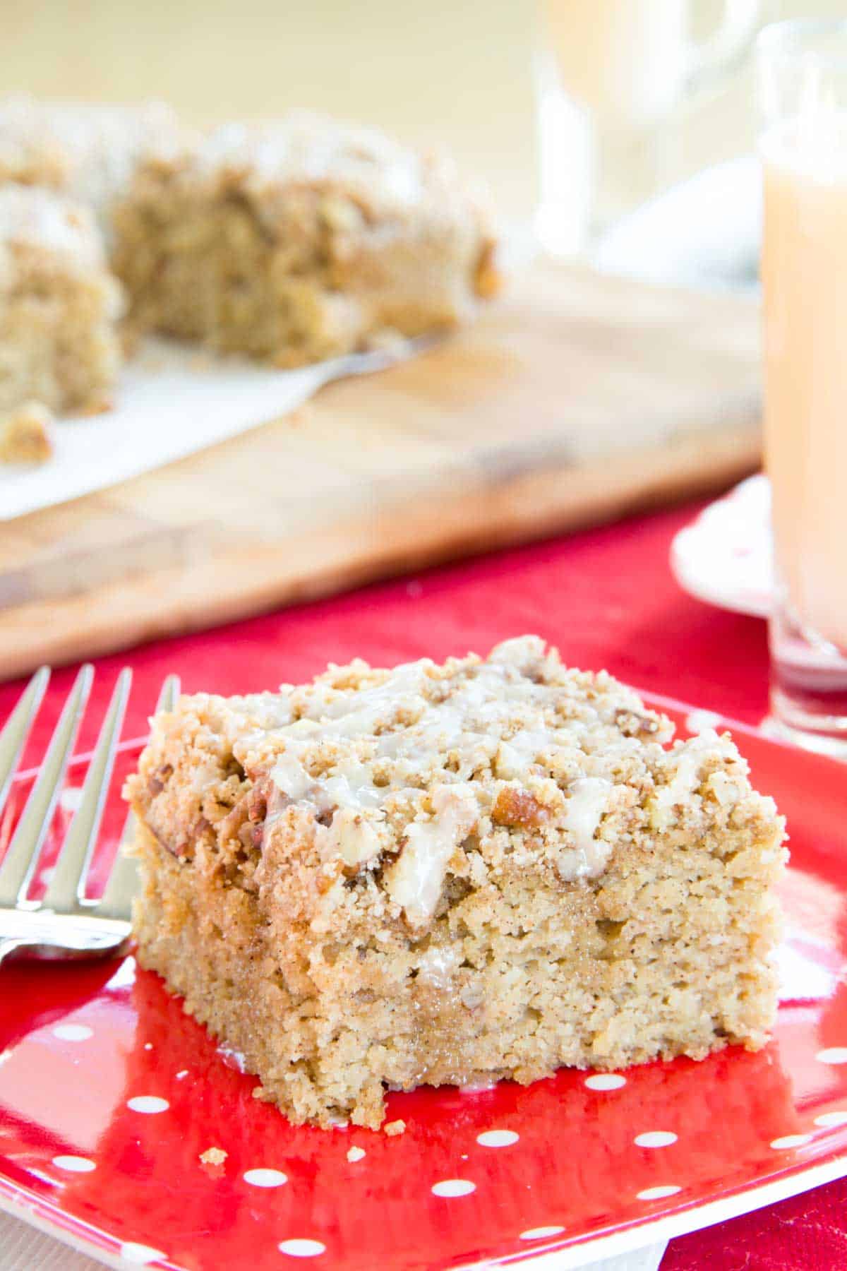 A piece of eggnog crumb cake on a red and white polka dot plate with more sliced on a cutting board in the background.