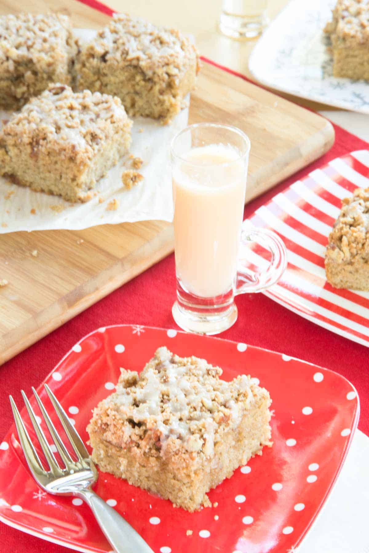 Looking down at a table with pieces of eggnog coffee cake on plates and a cutting board with one small glass of eggnog.