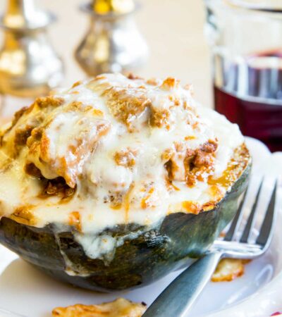 Half of an acorn squash studded with meat sauce and topped with mozzarella cheese on a plate with a fork.