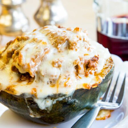 Half of an acorn squash studded with meat sauce and topped with mozzarella cheese on a plate with a fork.