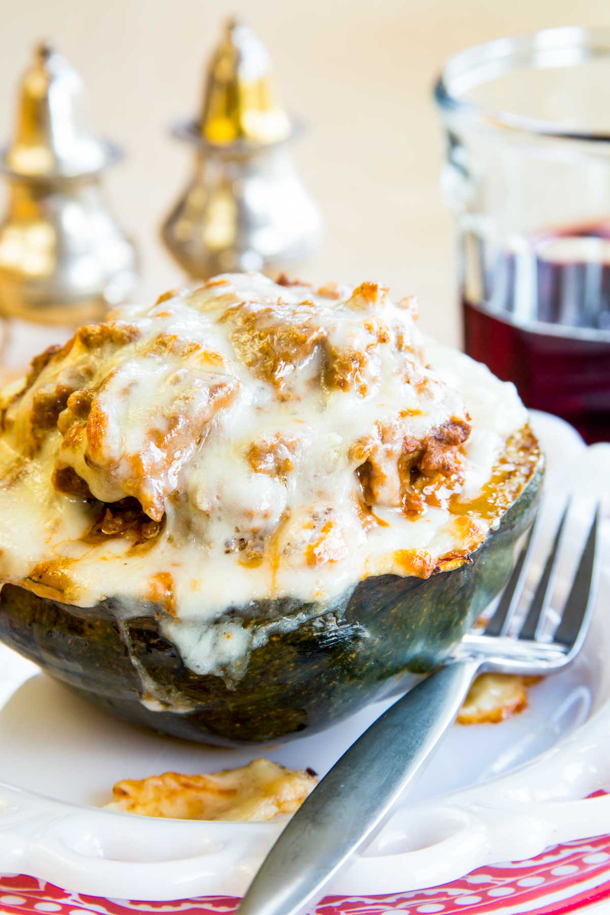 Half of an acorn squash studded with meat sauce and topped with mozzarella cheese on a plate with a fork.