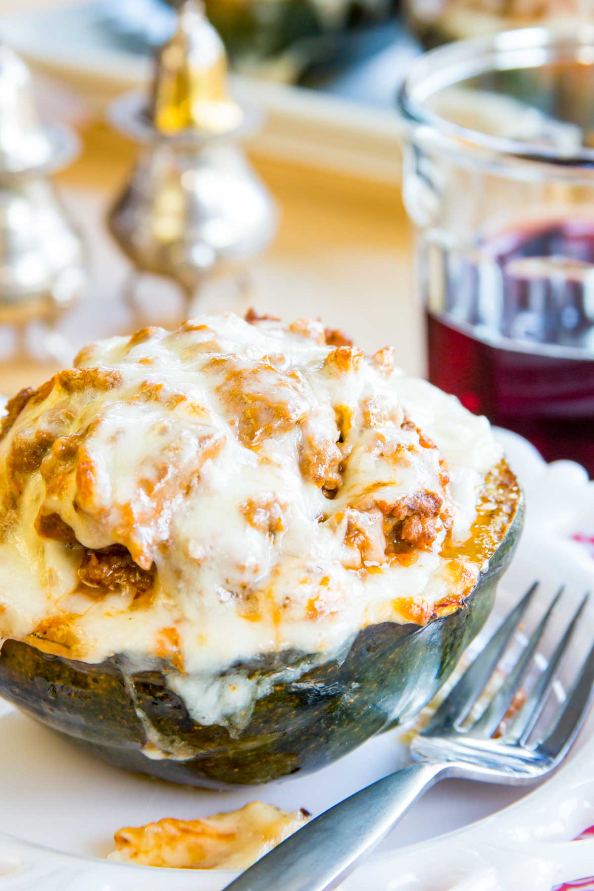 Stuffed acorn squash covered with melted mozzarella cheese on a white plate with a fork.