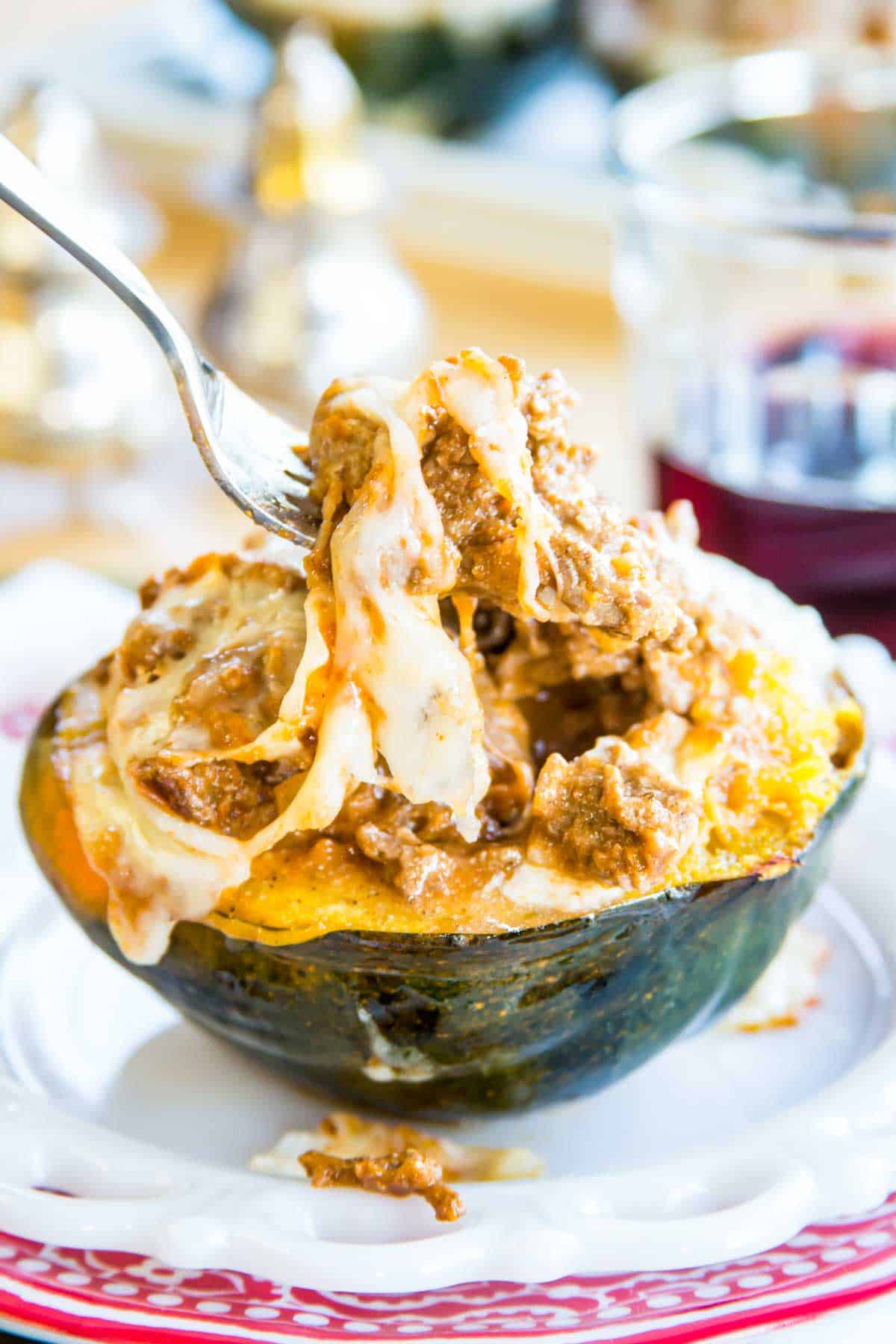 A fork picking up meat sauce and cheese out of a lasagna stuffed acorn squash half.