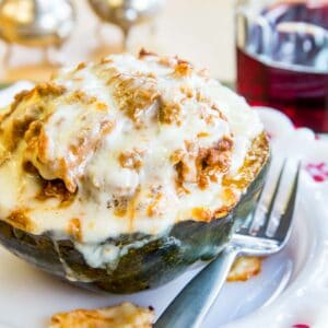 Lasagna stuffed acorn squash topped with melted mozzarella cheese on a white plate with a fork.