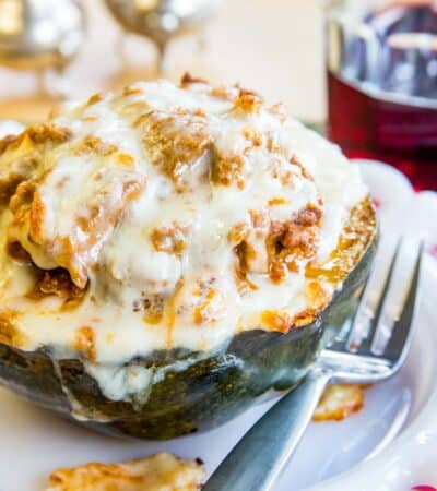 Lasagna stuffed acorn squash topped with melted mozzarella cheese on a white plate with a fork.