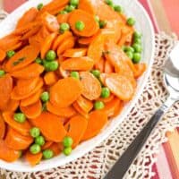 Browned Butter Peas and Carrots on a serving dish with a serving spoon on a striped placemat.