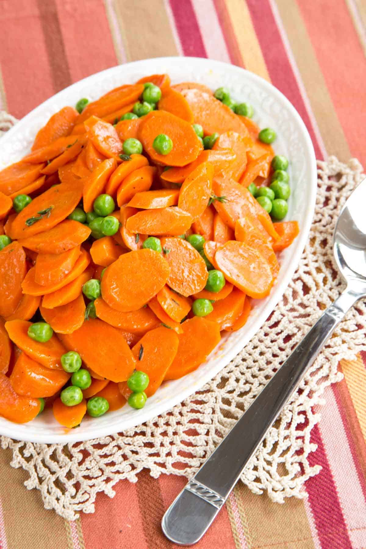 Browned Butter Peas and Carrots on a serving dish with a serving spoon on a striped placemat.