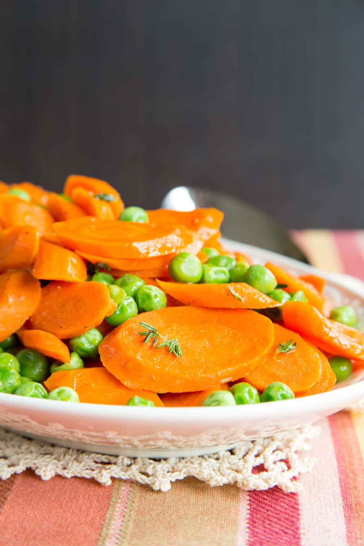 A dish of buttered peas and carrots sprinkled with thyme.