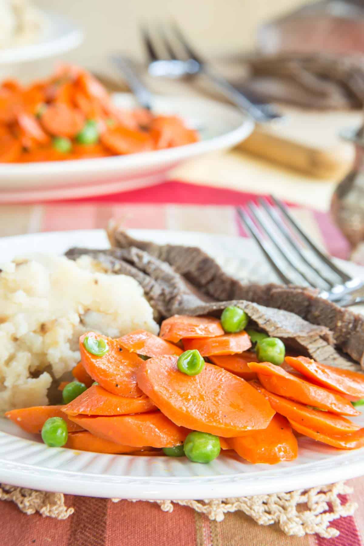 peas and carrots served on a plate with steak and mashed potatoes.