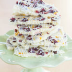 A small light green cake stand with a stack of pieces of Cranberry Bliss White Chocolate Bark.