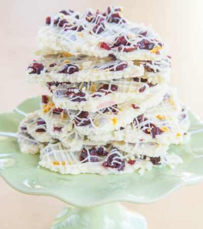 A small light green cake stand with a stack of pieces of Cranberry Bliss White Chocolate Bark.