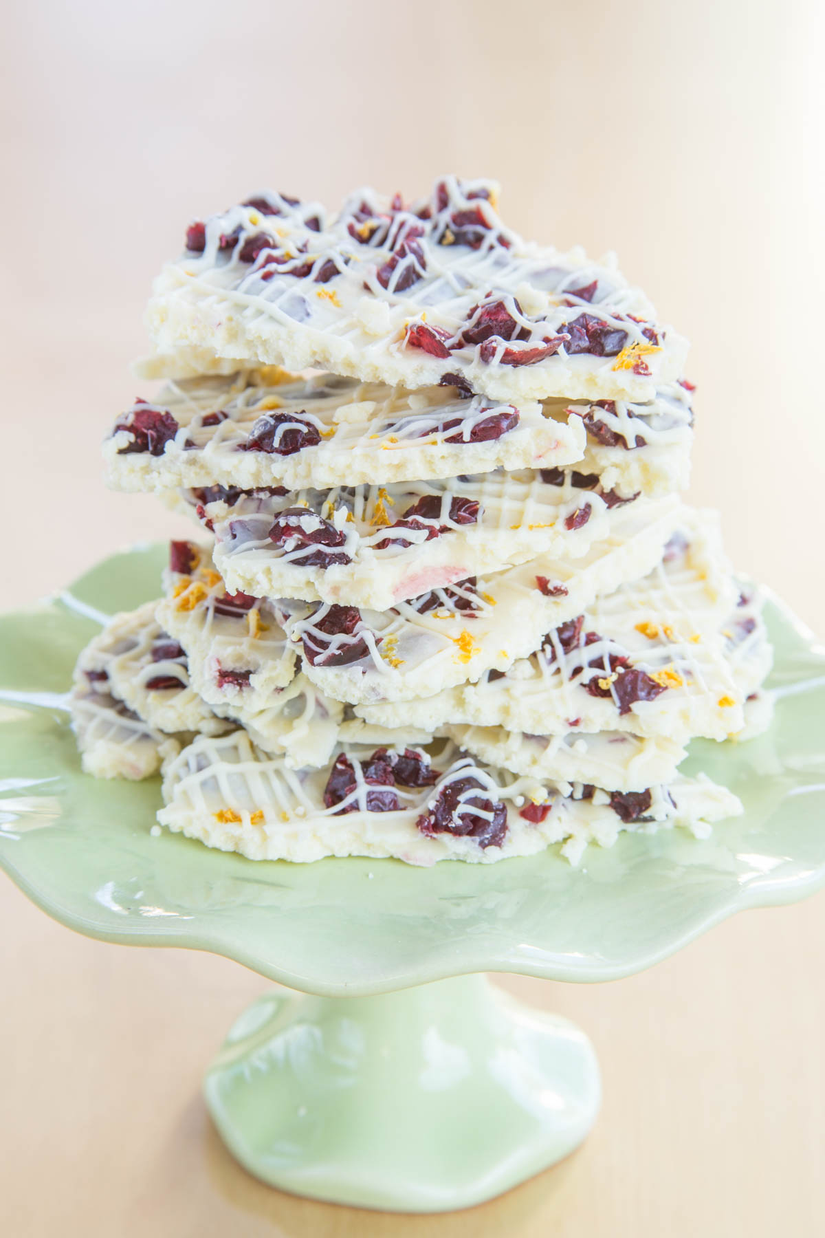 A small light green cake stand with a stack of pieces of Cranberry Bliss White Chocolate Bark.