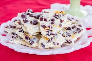 A white plate full of white chocolate bark with dried cranberries on a red tablecloth.
