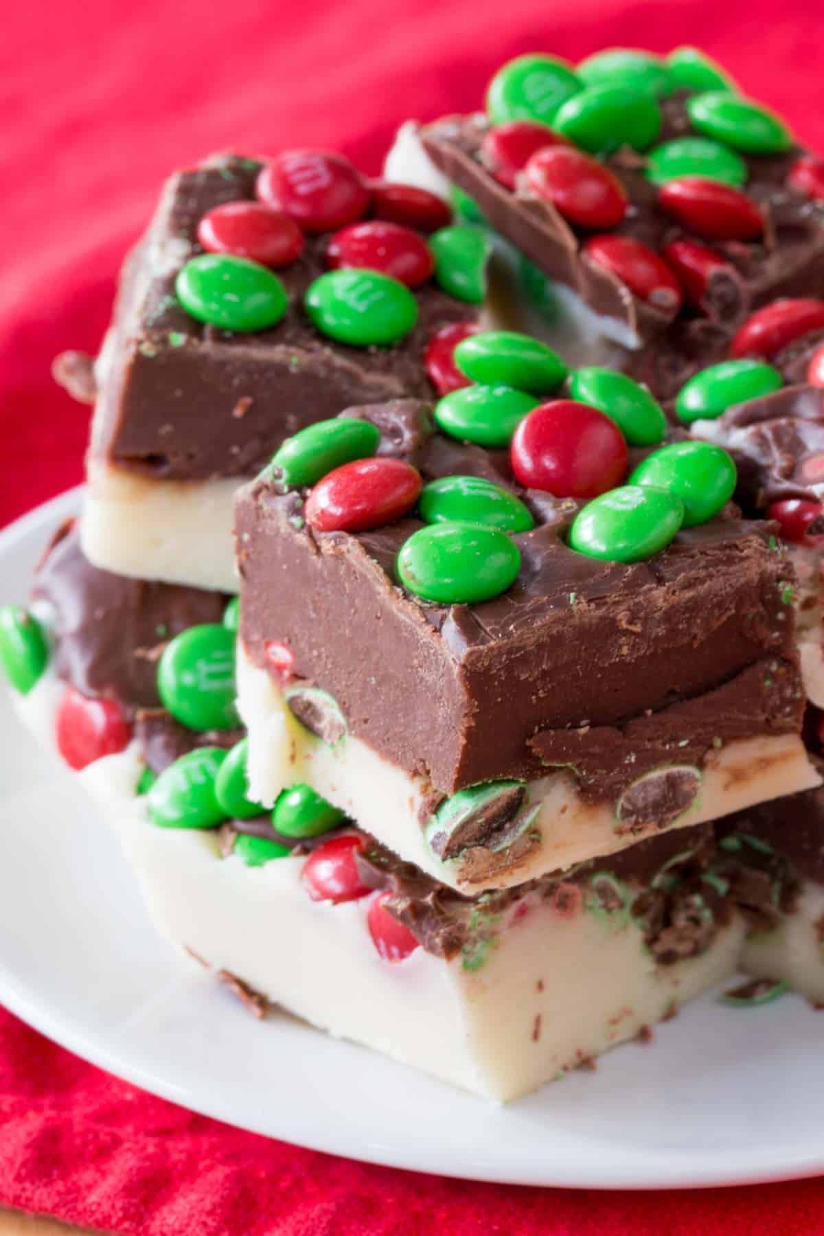 Two layer fudge with Holiday M&M's in it on a white plate on top of a red napkin.
