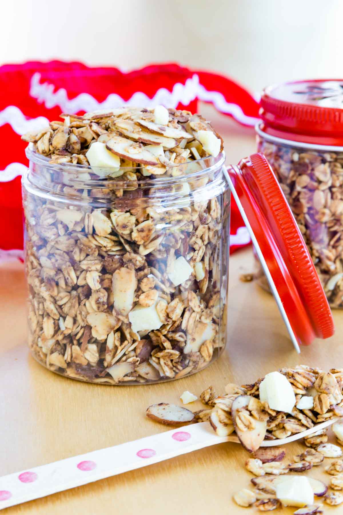 A small container of eggnog granola full of oats, almonds, and white chocolate with a red lid leaning against it.