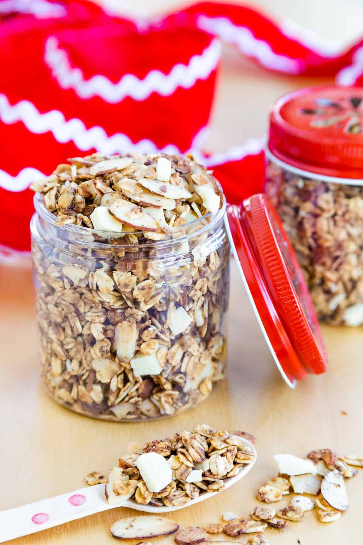 A jar of eggnog granola with red and white ribbon behind it and a spoon of granola in front of it.