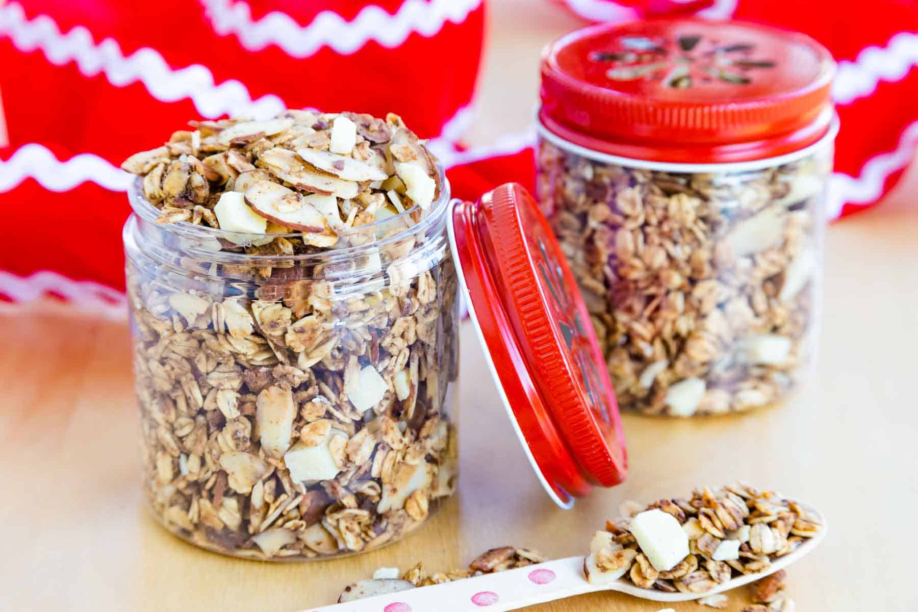 Two jars of eggnog granola, one with the lid off, and festive red and white ribbon coiled behind them.