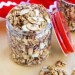 Eggnog Granola with pieces of white chocolate and sliced almonds and some in a spoon in front of the jar.