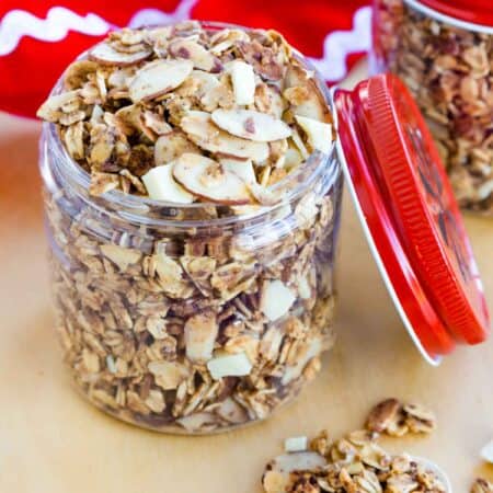 Eggnog Granola with pieces of white chocolate and sliced almonds and some in a spoon in front of the jar.