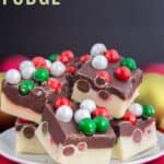 Dark and white chocolate layered fudge with holiday M&M's candies in it on a white plate on top of a red napkin with text overlay that says "Christmas Fudge".
