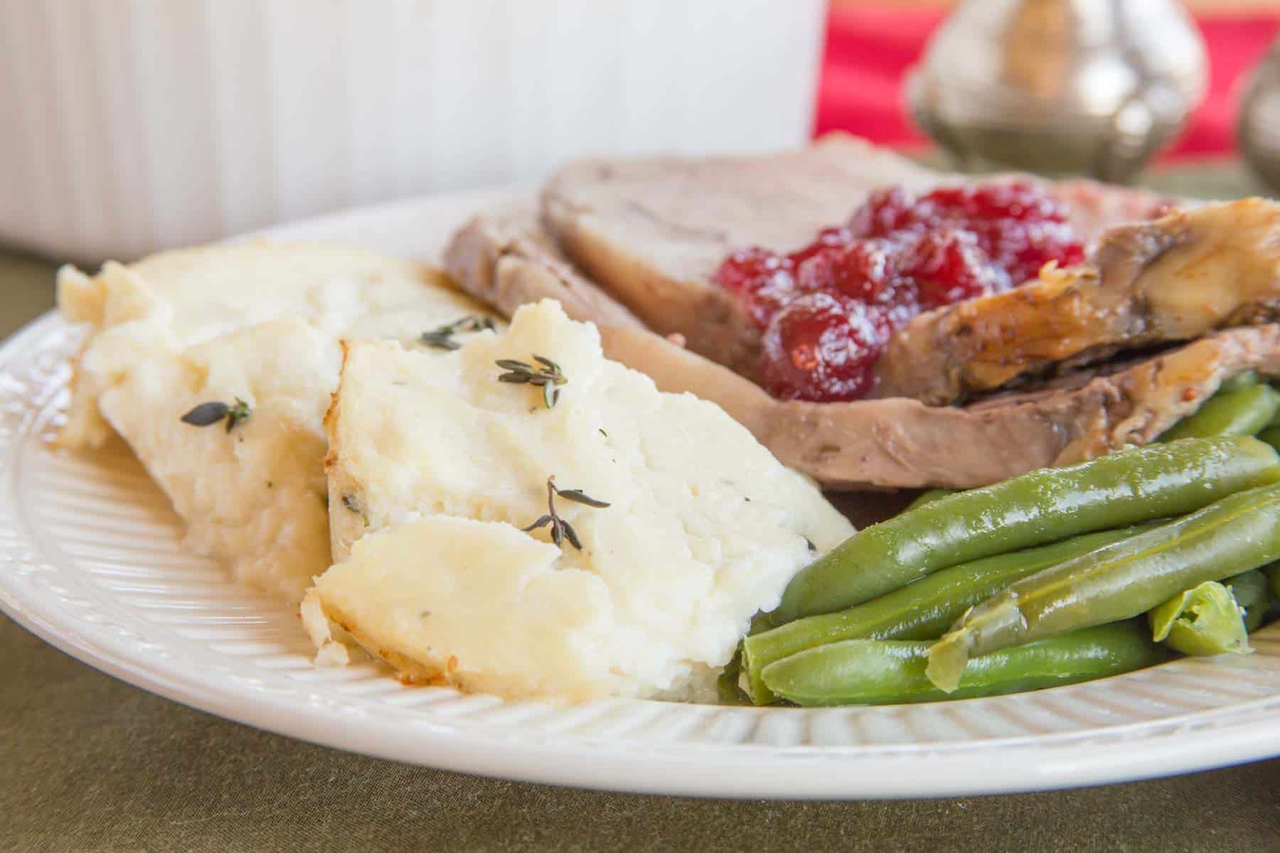 Creamy mashed cauliflower sprinkled with thyme served on a plate with green beans and a couple of slices of prime rib.