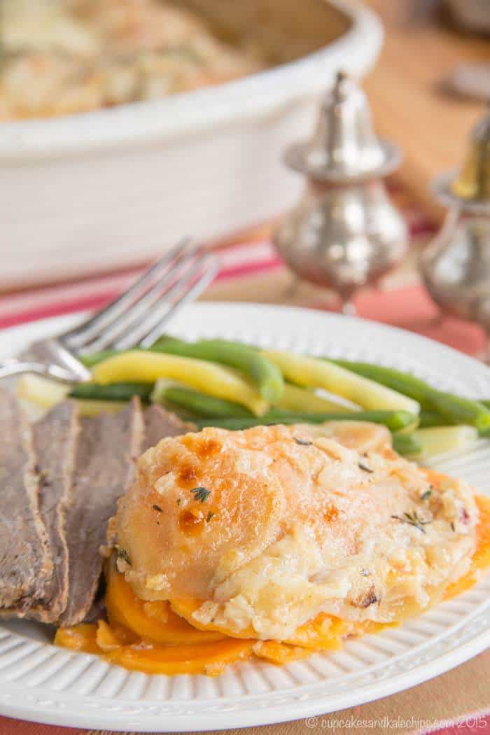 A serving of scalloped sweet potatoes on a plate with slices of beef and green beans