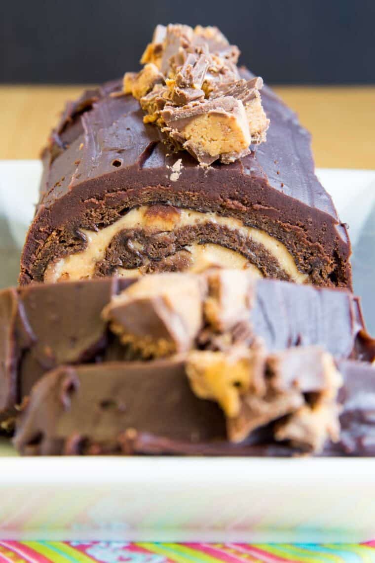 flourless chocolate cake roll with peanut butter filling and covered in chocolate ganahe and chopped Reese's on a serving plate