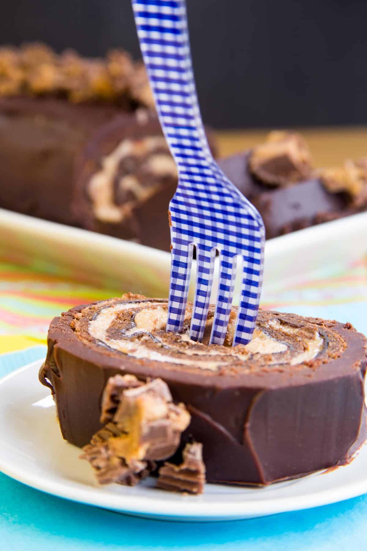 slice of flourless reese's chocolate cake roll on a plate with a blue and white fork in it