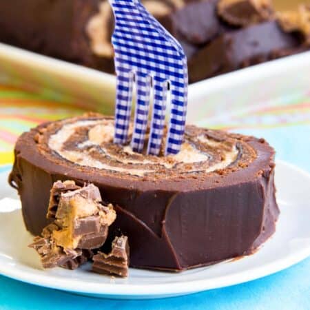 a fork standing up in a slice of the reese's chocolate cake roll on a plate