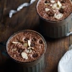 Two chocolate smoothies in glasses with sliced almonds and chocolate chips on top.