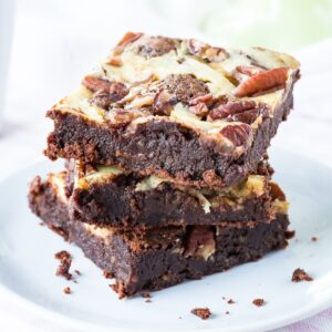 Three stacked turtle brownies with cheesecake swirl on a small white plate.
