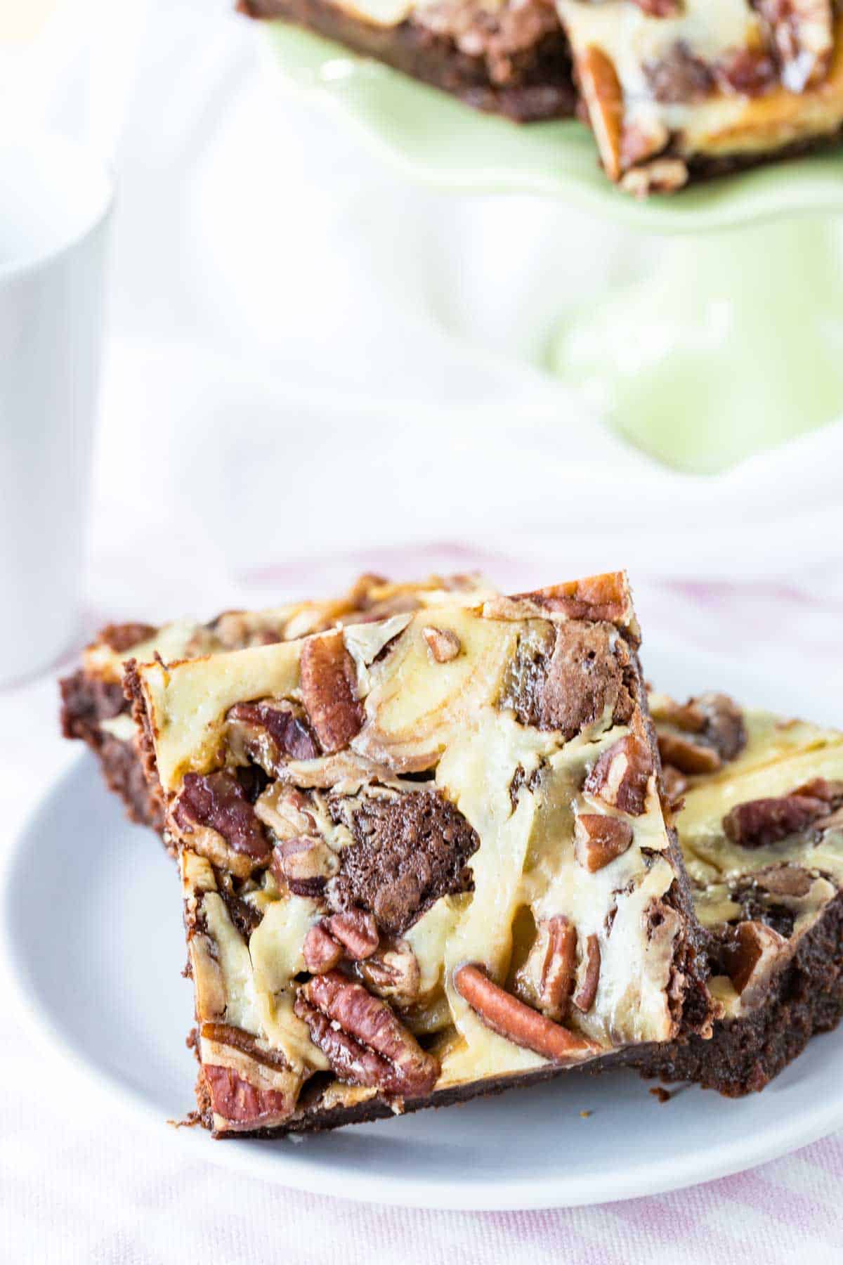 One turtle cheesecake brownie leaning against a couple more on a white plate.